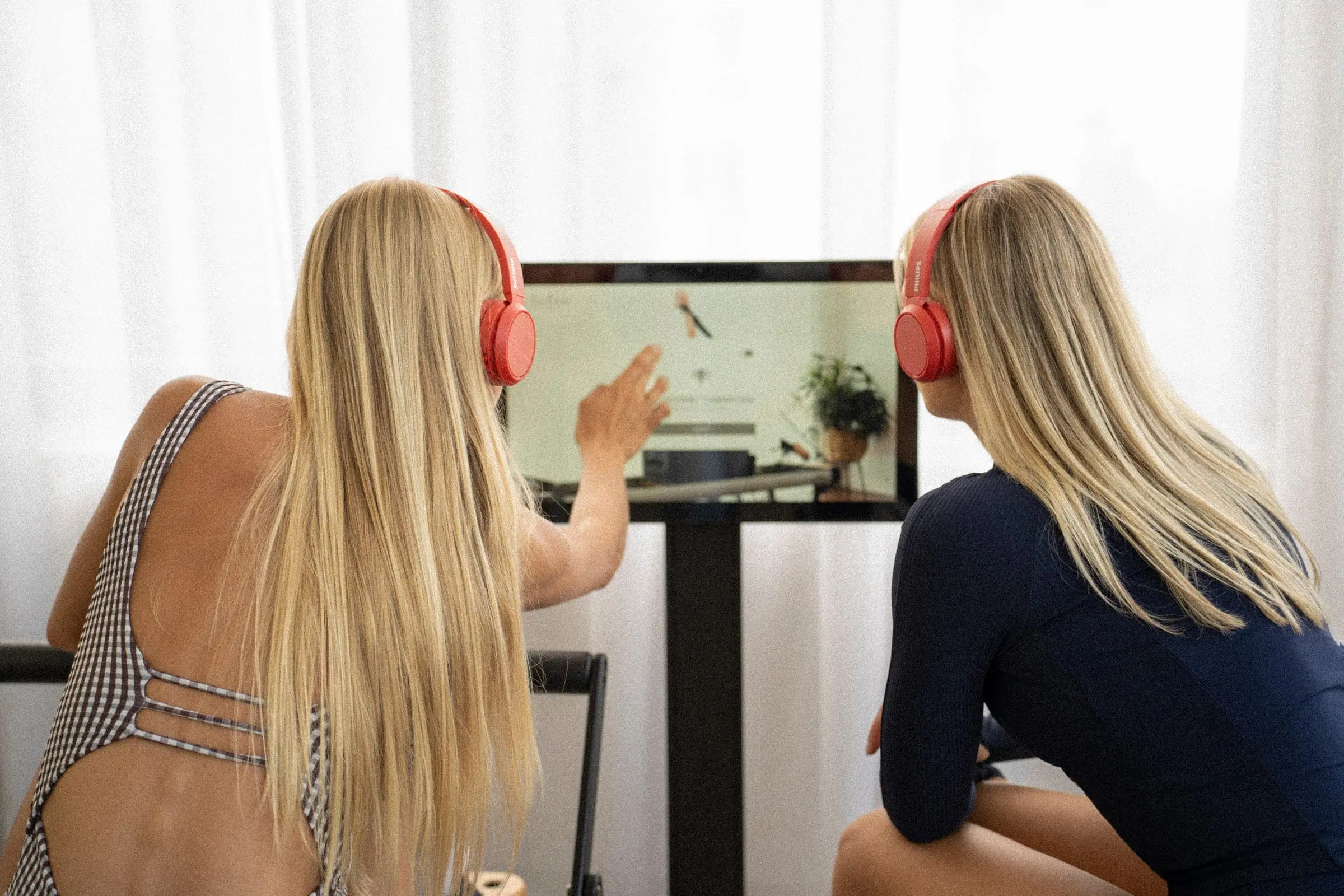 Dvi moterys su raudonomis ausinėmis žiūri į ekraną su virtualaus trenerio treniruote