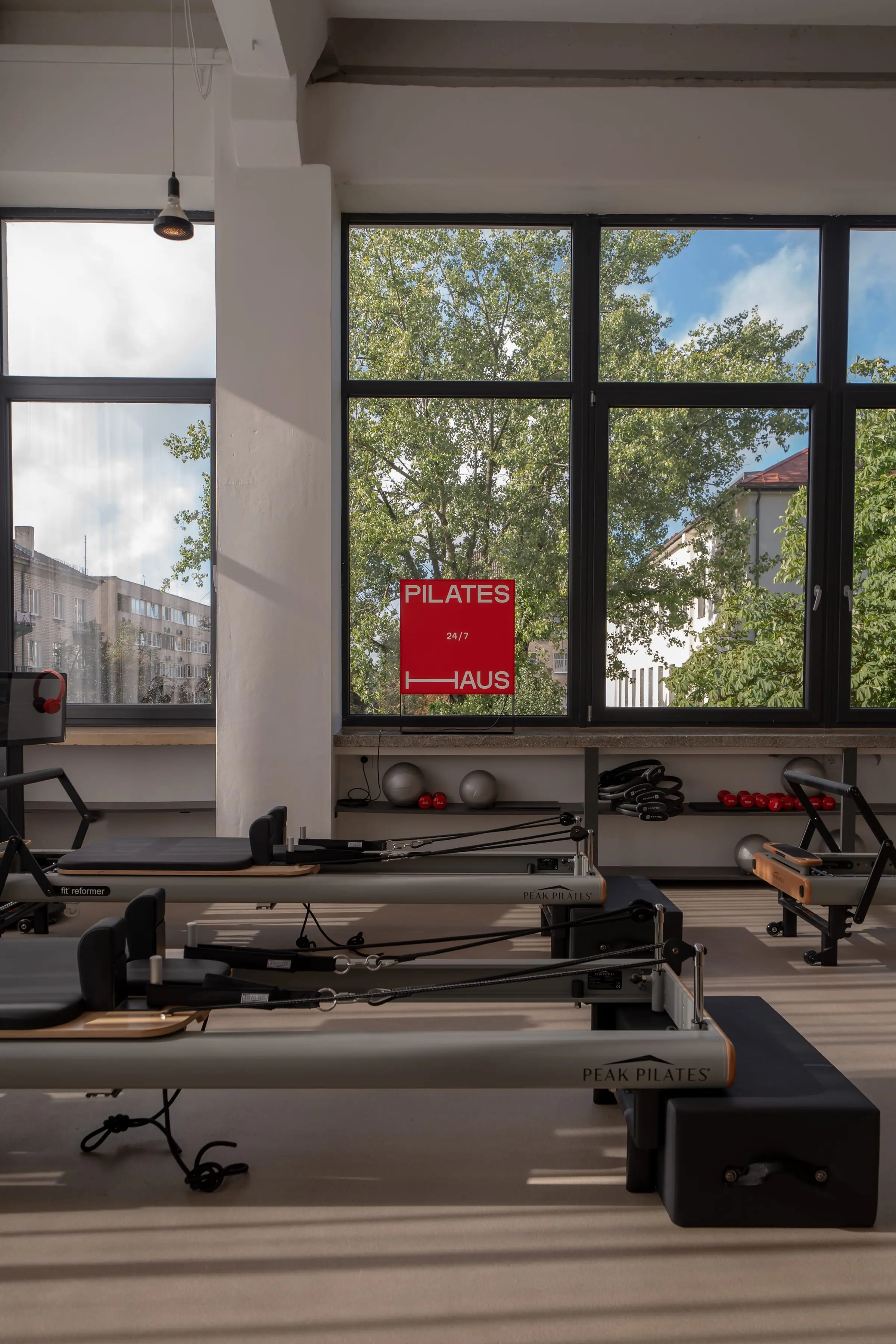 Reformer įranga prie lango su raudona Pilates Haus 24/7 iškaba